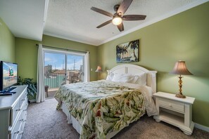 Une chambre à coucher avec un lit, un ventilateur de plafond, une table de chevet, une lampe, un téléviseur et une fenêtre donnant sur un beau paysage.