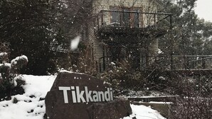 A snow-covered rock with the inscription "Tikkandi" in a natural setting with trees and a building in the background. - Tikkandi – Cozy Luxe Getaway in Victoria’s High Country (Merrijig)