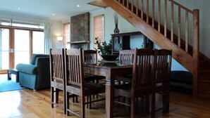 A dining area with a wooden table and chairs, a staircase, and a sofa in the background. - Tikkandi – Cozy Luxe Getaway in Victoria’s High Country (Merrijig)