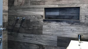 Een badkamer met een douche, een wastafel en een klein schap.