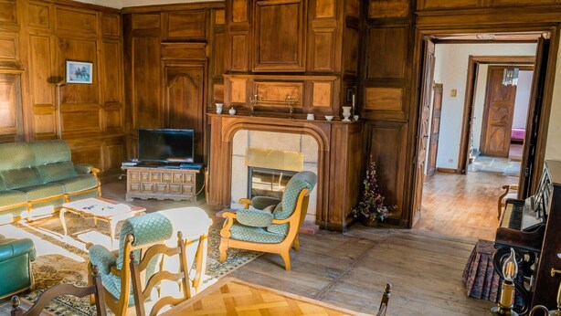 Un salon traditionnel avec des boiseries, une cheminée, un téléviseur et un piano.