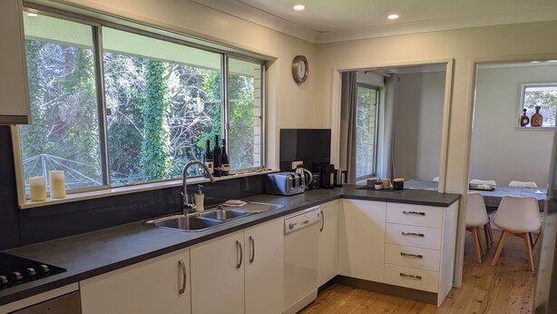 Eine moderne Küche mit einem großen Fenster, einem Geschirrspüler und einem Essbereich mit Tisch und Stühlen.