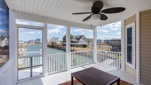 A covered porch with a ceiling fan, white railings, and a view of a river and houses. - Calypso by Seaside Vacations & Sales (Greenbackville)
