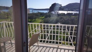 Un balcone con una sedia in vimini e un tavolo, affacciato su uno specchio d'acqua e sulla vegetazione.