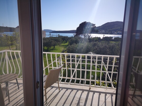 A balcony with a wicker chair and a table, overlooking a body of water and greenery.