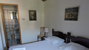 Un letto ben rifatto con lenzuola e cuscini bianchi, una testiera in legno, un comodino con una lampada e due quadri appesi al muro.