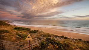 A coastal landscape with a beach, grassy dunes, and a wooden staircase leading down to the shore.