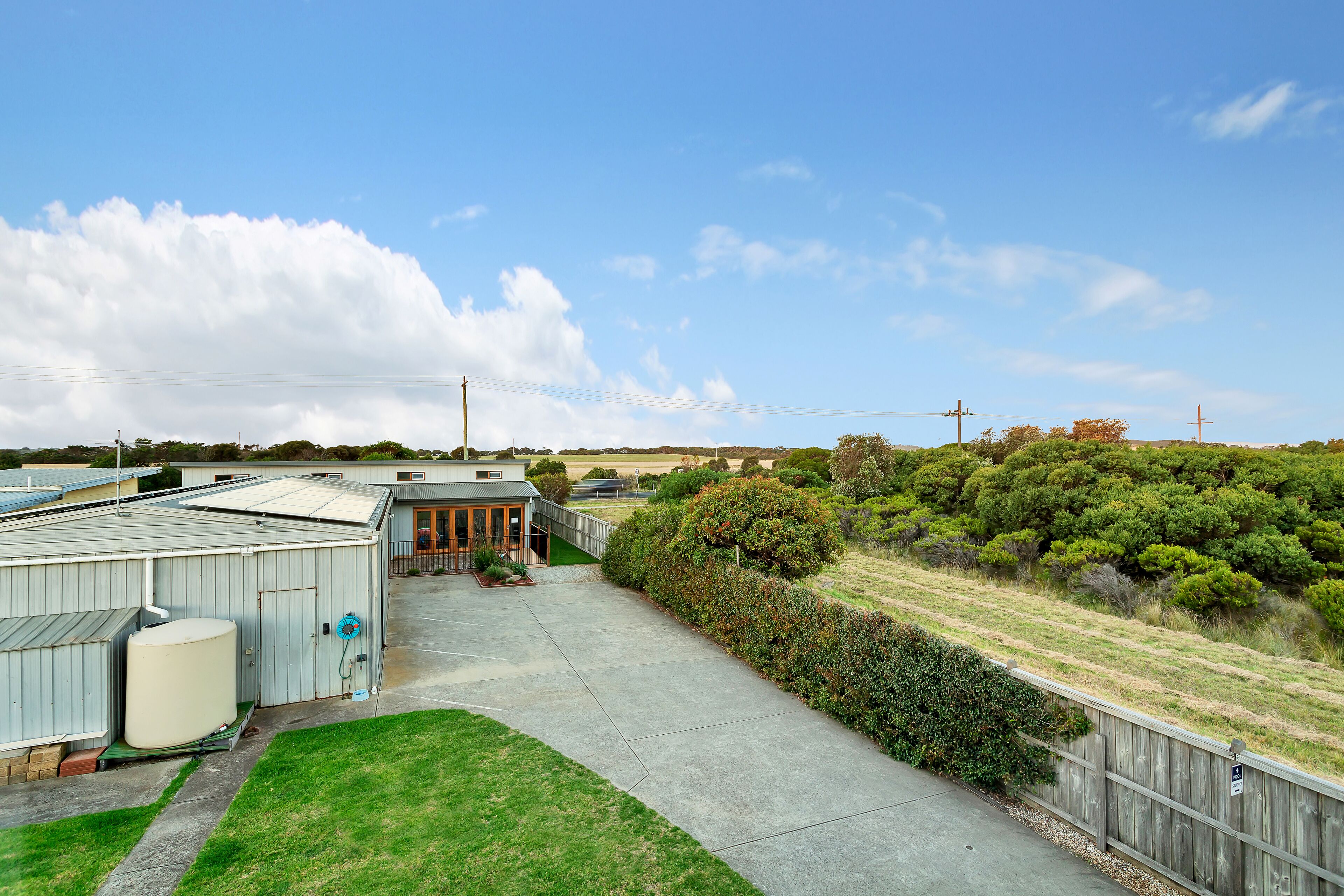 A residential area with a paved driveway leading to a house with a garage. There are green lawns and a wooden fence.