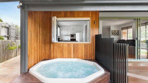 A modern outdoor hot tub area with a wooden wall and a view into a kitchen.