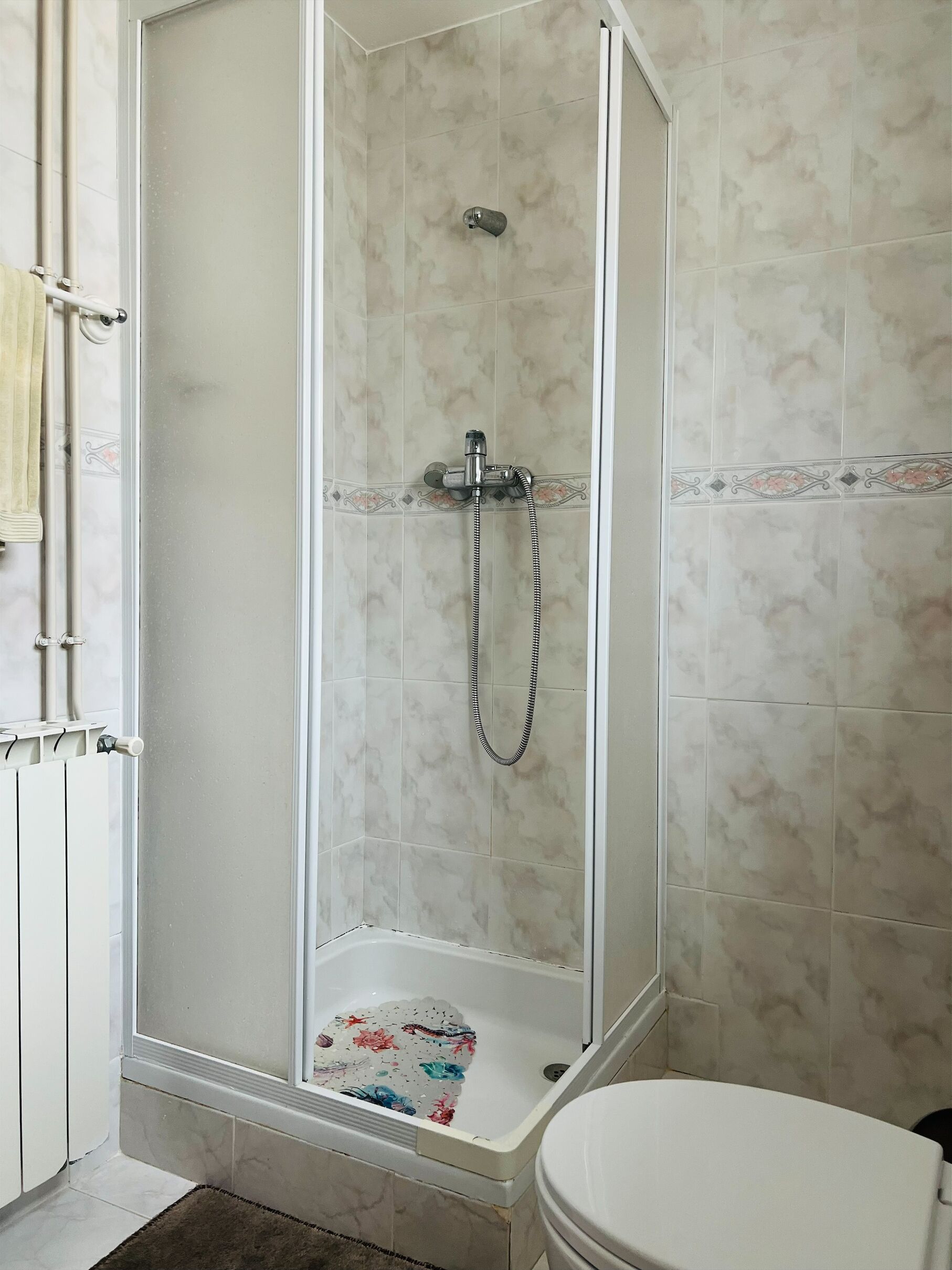 Une salle de bain équipée d’une douche, de toilettes et d’une baignoire agrémentée de tapis de bain à motifs floraux.