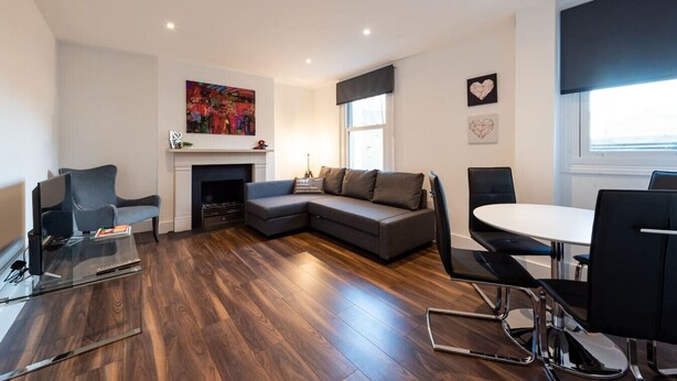 A modern living room with a sectional sofa, a glass coffee table, a fireplace, and a dining area with a round table and chairs. - Stunning Hyde Park Apartment (SS3) (London)