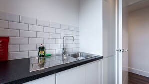 A modern kitchen with white cabinets, a black countertop, and a stainless steel sink. - Stunning Hyde Park Apartment (SS3) (London)