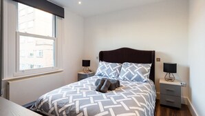 A bedroom with a bed, two bedside tables, a window, and a radiator. - Stunning Hyde Park Apartment (SS3) (London)