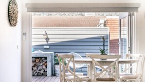 Une terrasse ouverte avec un ensemble de mobilier de jardin comprenant une table et des chaises, une lanterne, et une vue sur un mur de briques et un toit en tuiles.