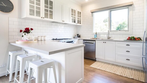 Une cuisine moderne avec des meubles blancs, un îlot central doté de tabourets, une cuisinière encastrée et un lave-vaisselle.