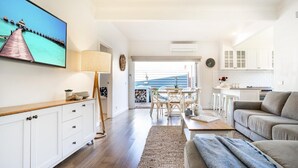 Un salon moderne avec un plancher en bois, un canapé, un téléviseur et un coin repas comprenant des chaises et une table.
