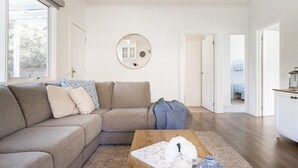 Un salon moderne avec un canapé d’angle, une table basse en bois et un grand miroir rond accroché au mur.