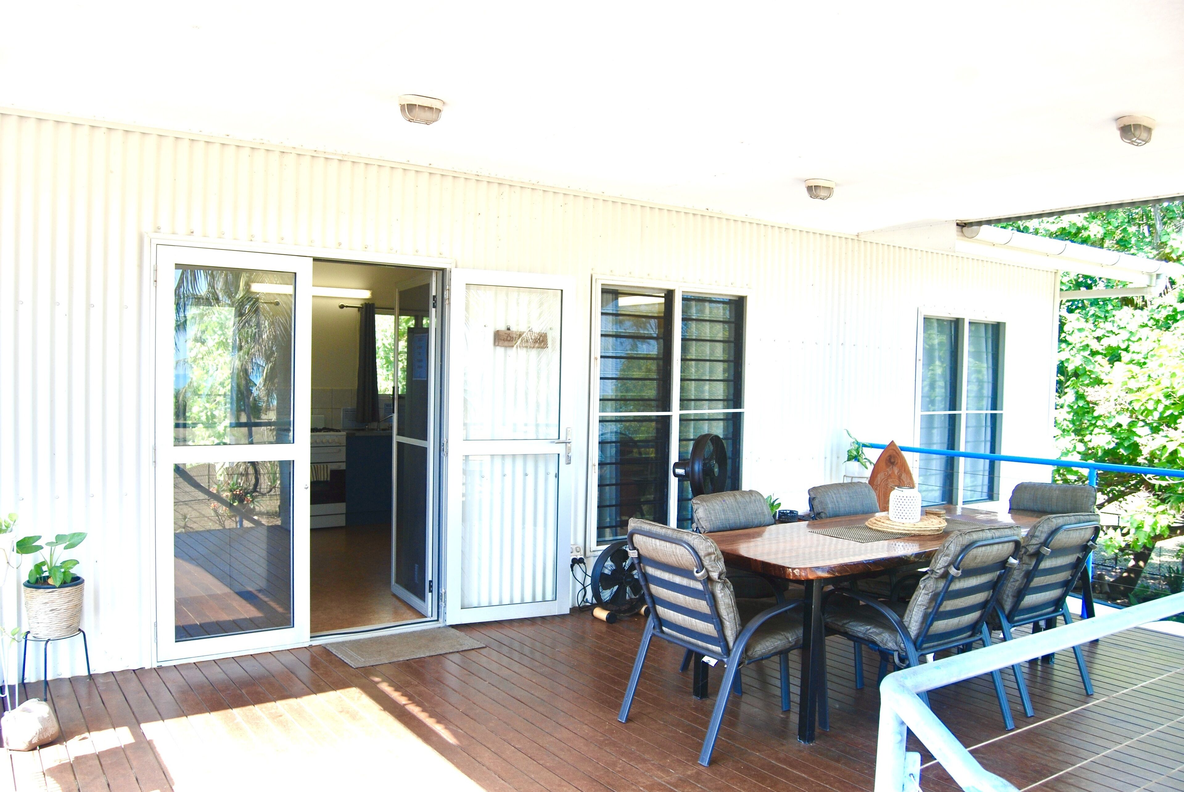 An outdoor patio with a wooden table and chairs, a sliding glass door leading to an interior space, and a small potted plant.