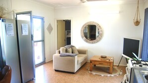 Un espacio habitable compacto con kitchenette, un sofá, una mesa de centro y un espejo redondo en la pared.