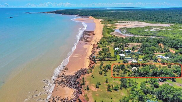 Vista aérea de una zona costera con playa, vegetación verde y un terreno delimitado.