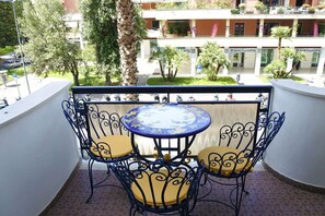 A balcony with a round table and four chairs, overlooking a street with parked cars and a building with 'BANCO DI NAPOLI' signage.