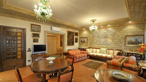 A spacious living room with a large sofa set, a dining table with chairs, a TV, and a decorative chandelier.