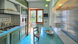 A kitchen with a stove, oven, and microwave, a dining table with a chair, and a view through a window.