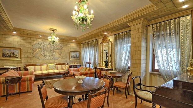 A spacious living room with a round dining table, multiple chairs, a sofa set, and a piano.