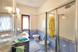 A bathroom with a glass shower enclosure, a sink with a mirror, a toilet, and a window with a curtain.