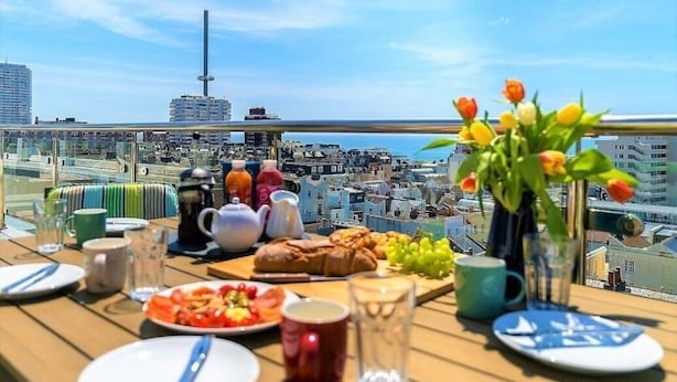 Una mesa dispuesta con alimentos para el desayuno y un jarrón de tulipanes en un balcón con vistas a un paisaje urbano.