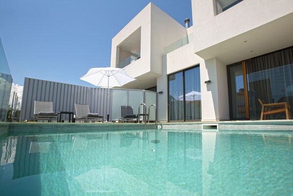 A modern pool area with clear water, a white umbrella, and lounge chairs.