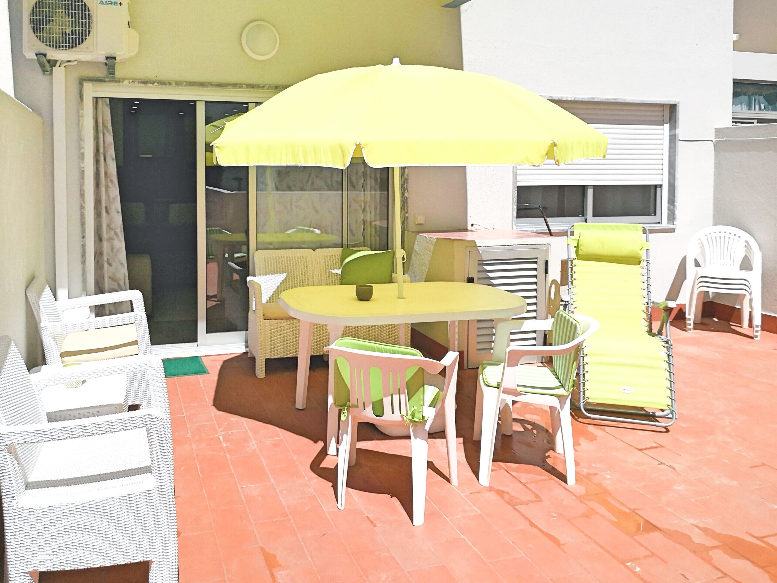 Une terrasse avec un parasol jaune, des meubles en osier et une chaise blanche.