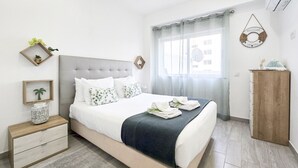 Un dormitorio ordenado con cama, mesitas de noche, armario y ventana con cortinas.