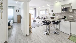 Una cocina moderna con armarios blancos, un microondas de acero inoxidable y una zona con taburetes de bar.