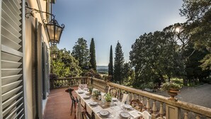 An outdoor dining area with a table set for four, overlooking a garden with trees and a view of the countryside. - Villa Belvedere in the heart of Chianti (loro ciuffenna)
