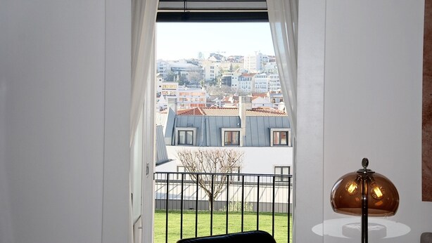 Quarto com vista para a cidade através de uma janela com cortinas brancas.