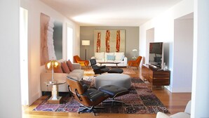 Uma sala de estar moderna com um sofá, cadeiras, uma mesa de centro e uma televisão.