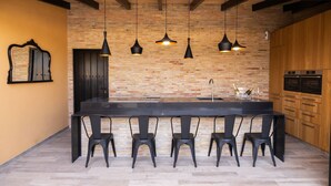 A modern kitchen with a brick wall, wooden cabinets, a black countertop, and four black chairs. - HOUSE IN THE EBRO DELTA, WITH WIFI, HEATED POOL, PARKING AND BARBECUE. (Deltebre)