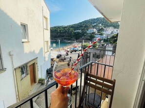 A balcony with a clear view of a beach, a railing, and a glass table with a drink.