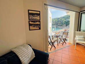 A balcony with a view of the sea, a dining area with chairs and tables, and a sofa with striped pillows.