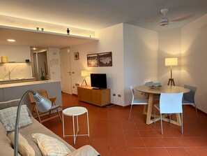 Un soggiorno moderno con un divano, un tavolo da pranzo con sedie, una televisione e un angolo cottura con lavello e pensili.