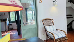 Una habitación con una mesa de comedor, una silla de mimbre con cojín a rayas, el número '3' en la pared, una zona de cocina con microondas y una escalera.