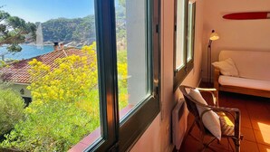 Habitación con un amplio ventanal que ofrece vistas a la costa, un sofá blanco y una silla de mimbre.