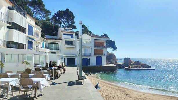 Un edificio frente al mar con terraza al aire libre, vista a la playa y un promontorio rocoso.