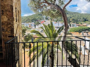 Un balcon avec un mur en pierre, des palmiers et une vue sur une ville avec des bâtiments et une colline en arrière-plan.