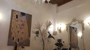 Ein Essbereich mit einer Deckenleuchte, einem Tisch mit weißer Spitze, weißen Stühlen und einem Gemälde an der Wand.