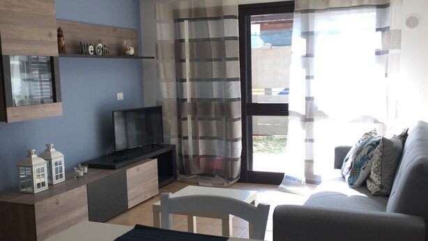 A modern living room with a grey sofa, a dining table with a white tablecloth, and a TV on a wooden cabinet.