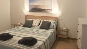 A neatly made bed with striped bedding, a bedside table with a lamp, and a wall-mounted air conditioner.