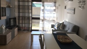 A modern kitchen with a dining area, a sofa, and a view through a glass door.