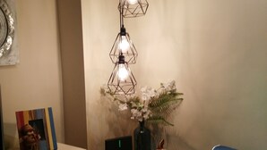 Une pièce avec une table en verre, une chaise bleue, un meuble blanc et un luminaire fixé au mur.